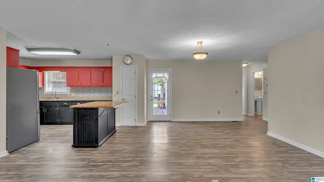 kitchen with light wood-style floors, freestanding refrigerator, a sink, baseboards, and backsplash