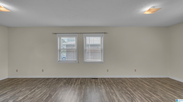empty room with dark wood-type flooring, visible vents, and baseboards