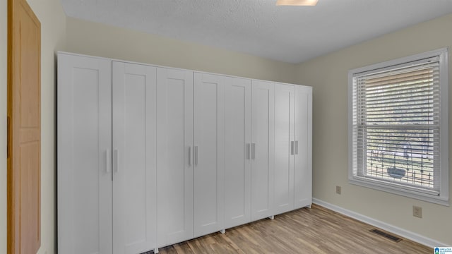 unfurnished bedroom featuring a closet, light wood-type flooring, baseboards, a textured ceiling, and visible vents