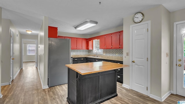 kitchen with a sink, wooden counters, freestanding refrigerator, and light wood-style floors