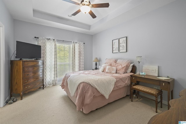 bedroom with a raised ceiling, light carpet, and ceiling fan