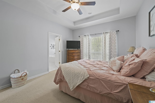 bedroom featuring baseboards, a raised ceiling, connected bathroom, ceiling fan, and light colored carpet