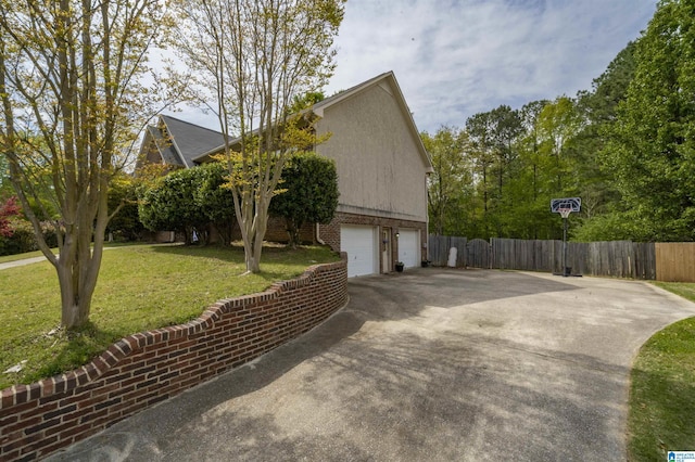 view of property exterior with a yard, a garage, fence, brick siding, and driveway