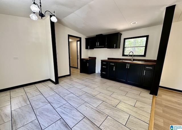 kitchen featuring dark cabinets, a sink, lofted ceiling, baseboards, and a notable chandelier