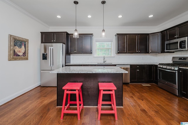 kitchen with stainless steel appliances, backsplash, a sink, a kitchen island, and crown molding