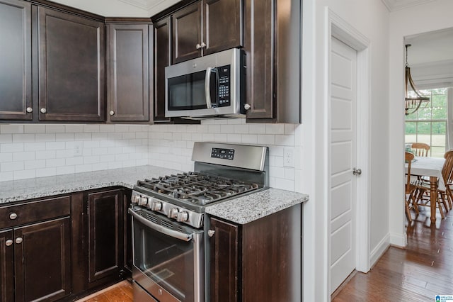 kitchen with wood finished floors, ornamental molding, dark brown cabinetry, and stainless steel appliances