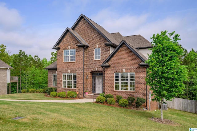 traditional-style home with fence, brick siding, a front yard, and central air condition unit