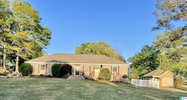 view of front facade featuring a detached garage, a front lawn, brick siding, an outbuilding, and fence
