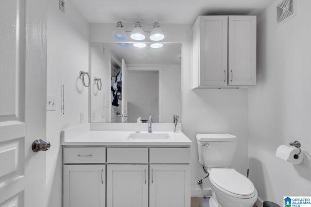 half bathroom with vanity, visible vents, baseboards, and toilet