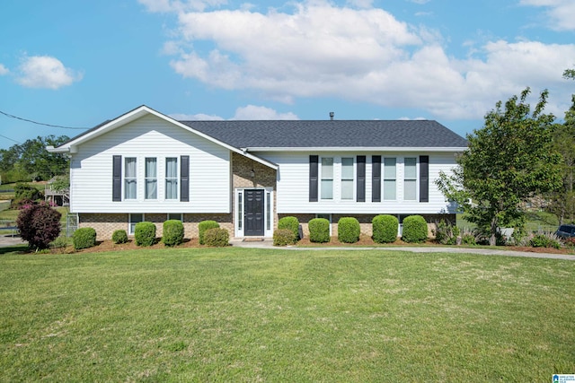 raised ranch with roof with shingles, brick siding, and a front lawn
