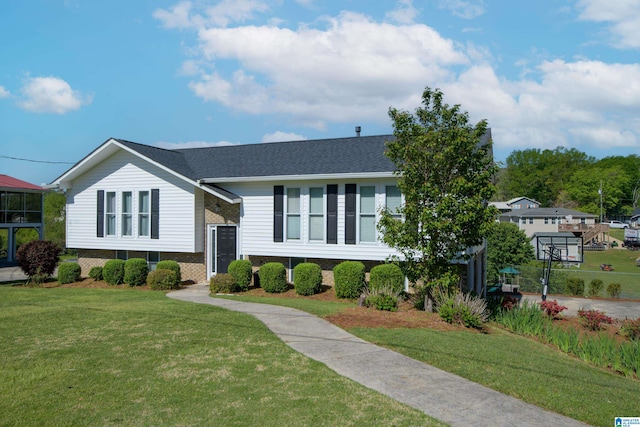 split foyer home with a shingled roof, brick siding, and a front yard