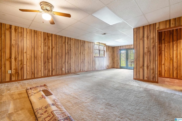 interior space featuring baseboards, carpet flooring, wood walls, visible vents, and a drop ceiling