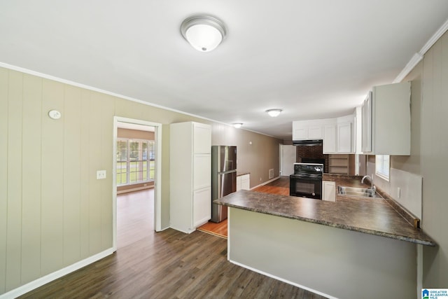 kitchen featuring black / electric stove, a peninsula, freestanding refrigerator, dark wood-type flooring, and a sink