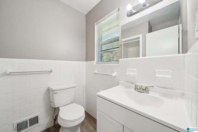 bathroom featuring visible vents, toilet, tile walls, vanity, and wood finished floors