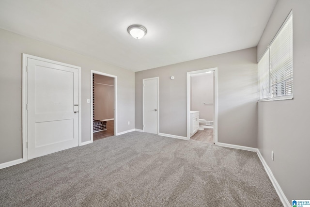 unfurnished bedroom with ensuite bathroom, baseboards, a walk in closet, and carpet flooring