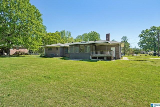 rear view of property featuring cooling unit, a sunroom, a yard, brick siding, and a chimney