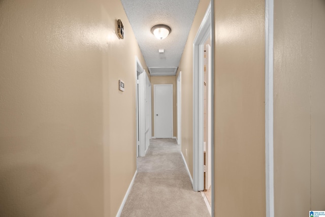 hall with light carpet, baseboards, and a textured ceiling