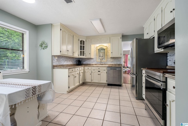 13563 Date St, Northport, AL 35475 - kitchen featuring a sink, light tile patterned floors, backsplash, a textured ceiling, and appliances with stainless steel finishes