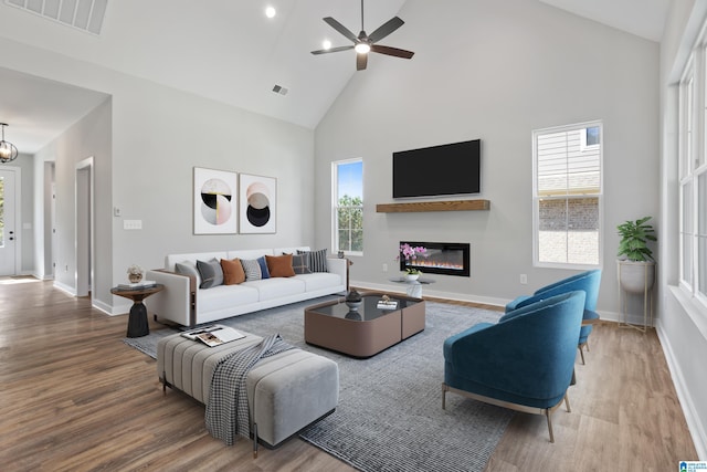 living area featuring visible vents, high vaulted ceiling, a glass covered fireplace, and wood finished floors