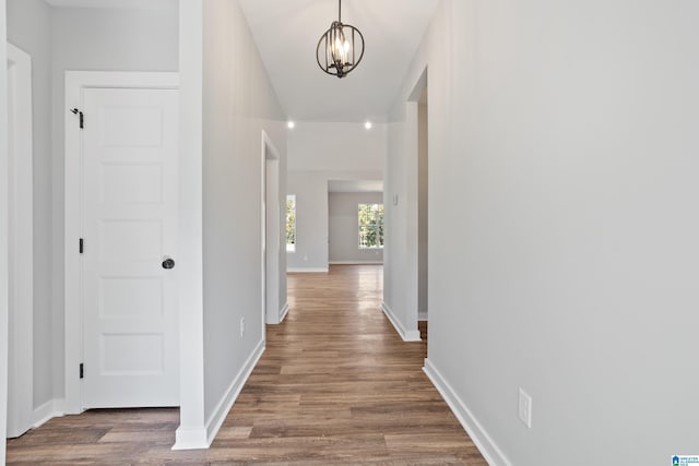 corridor with baseboards, a notable chandelier, and dark wood-style floors