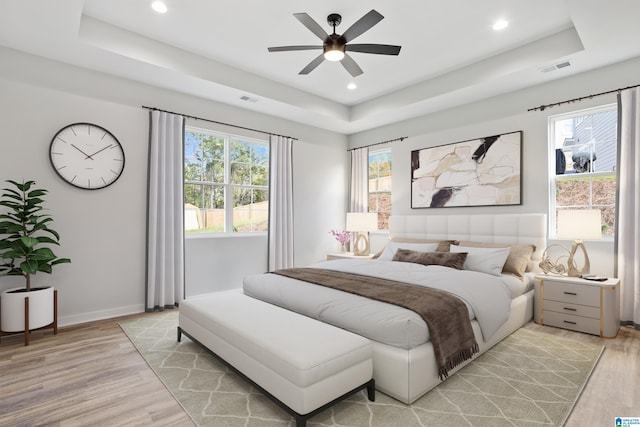 bedroom featuring a raised ceiling, recessed lighting, baseboards, and light wood-style flooring