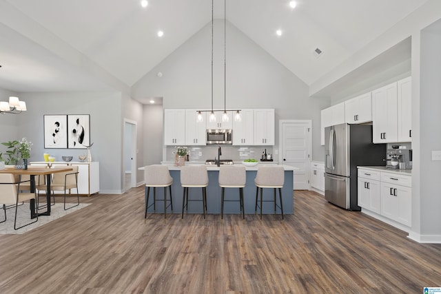 kitchen featuring an island with sink, a chandelier, a kitchen bar, stainless steel appliances, and high vaulted ceiling