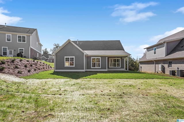 rear view of property with cooling unit, a shingled roof, and a lawn