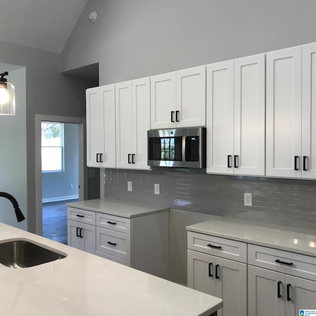 kitchen with a sink, light countertops, stainless steel microwave, white cabinetry, and backsplash