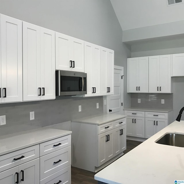 kitchen featuring stainless steel microwave, white cabinets, a sink, and backsplash