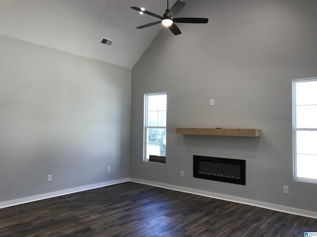 unfurnished living room with a glass covered fireplace, dark wood-style floors, visible vents, ceiling fan, and high vaulted ceiling