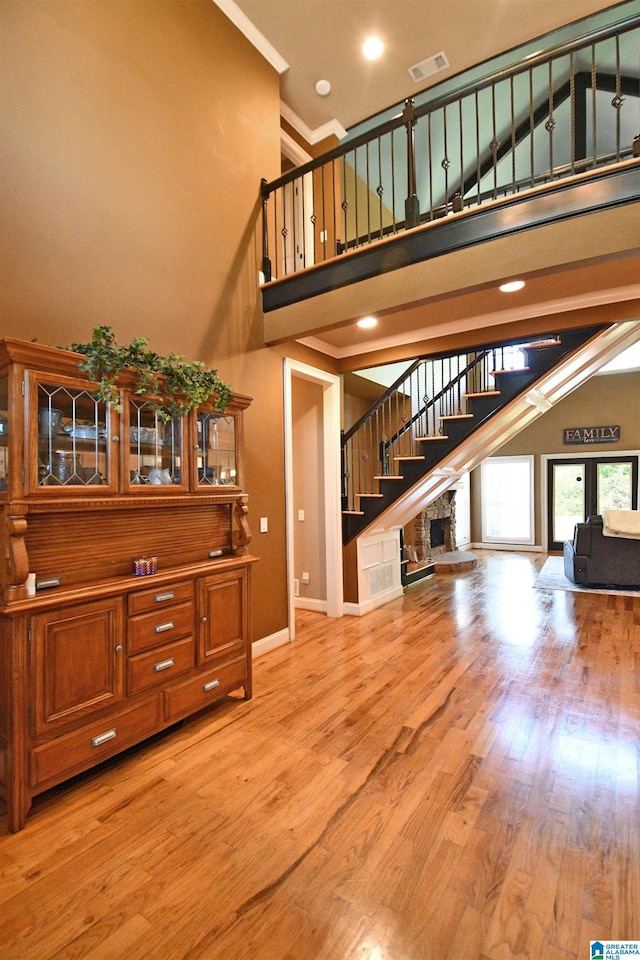 unfurnished living room featuring stairs, light wood-style floors, baseboards, a high ceiling, and visible vents