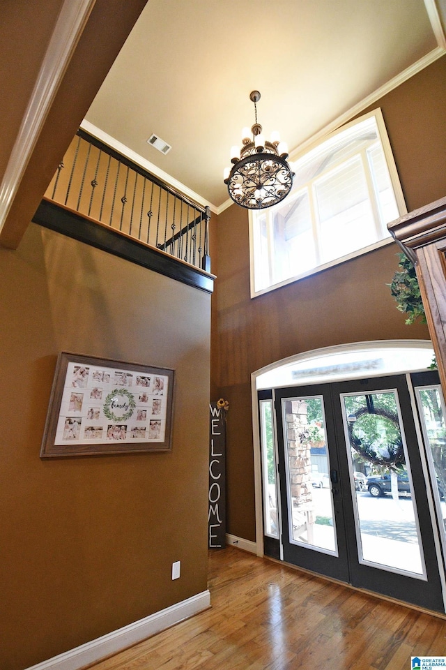 foyer featuring french doors, visible vents, an inviting chandelier, wood finished floors, and crown molding