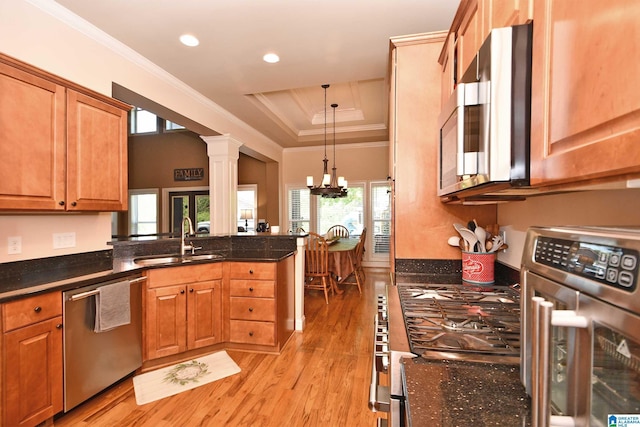 kitchen with stainless steel appliances, a peninsula, a sink, light wood-type flooring, and ornamental molding