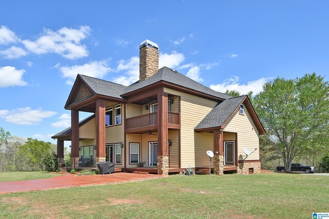 back of property with a chimney, a yard, a balcony, and a shingled roof