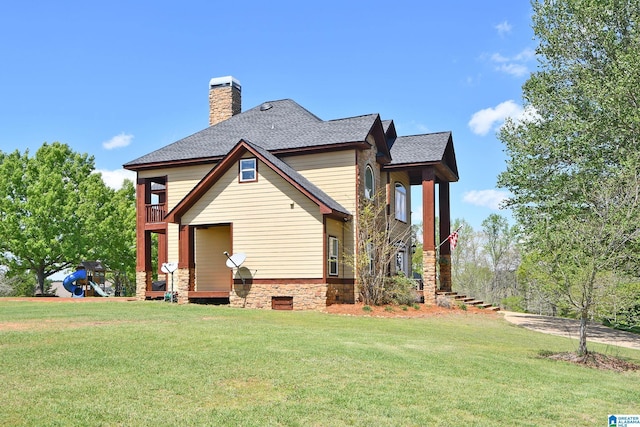 back of house with a chimney, roof with shingles, a yard, and a balcony