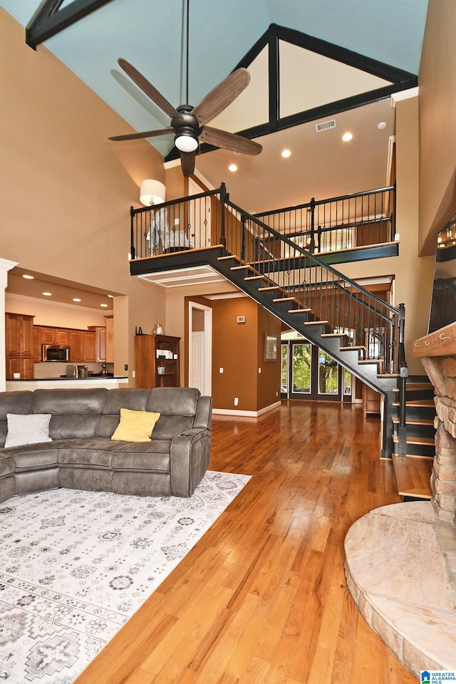living area featuring visible vents, a high ceiling, stairway, ceiling fan, and hardwood / wood-style floors
