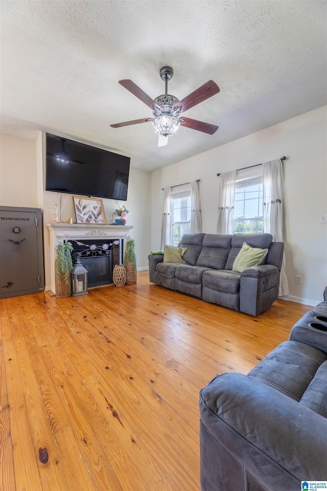 living room with a fireplace, wood finished floors, a textured ceiling, and ceiling fan