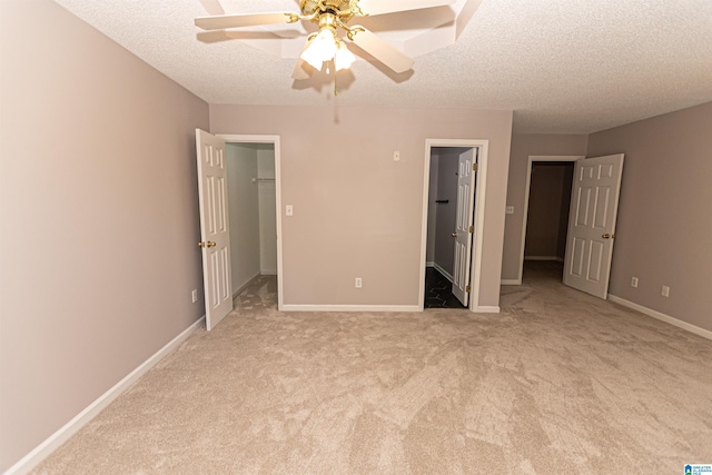 unfurnished bedroom featuring a walk in closet, a textured ceiling, baseboards, a closet, and light carpet