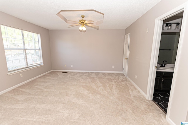 empty room featuring ceiling fan, light carpet, a sink, a textured ceiling, and baseboards