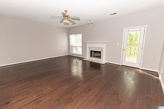 unfurnished living room featuring plenty of natural light, a ceiling fan, dark wood finished floors, and visible vents