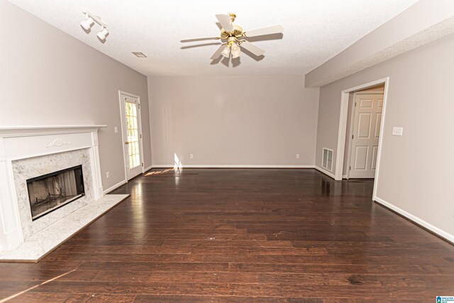 unfurnished living room featuring ceiling fan, a textured ceiling, visible vents, a high end fireplace, and wood finished floors