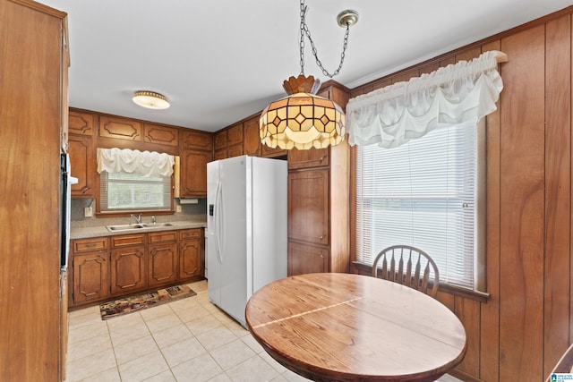 kitchen with light tile patterned floors, white refrigerator with ice dispenser, light countertops, brown cabinetry, and a sink