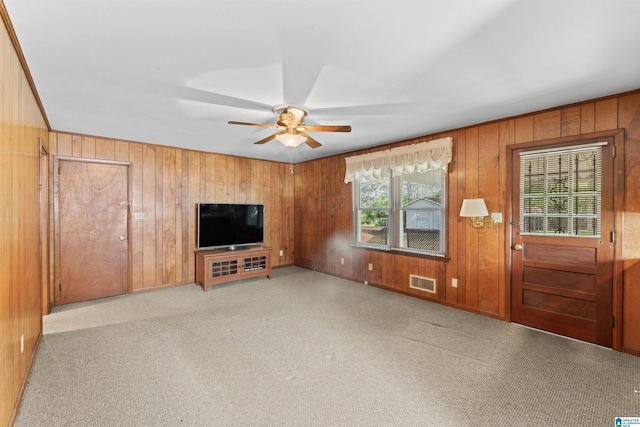 unfurnished living room with visible vents, a ceiling fan, carpet flooring, and wood walls