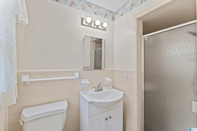 bathroom with vanity, toilet, a shower stall, wainscoting, and tile walls