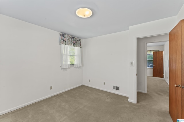spare room featuring light carpet, a healthy amount of sunlight, baseboards, and visible vents