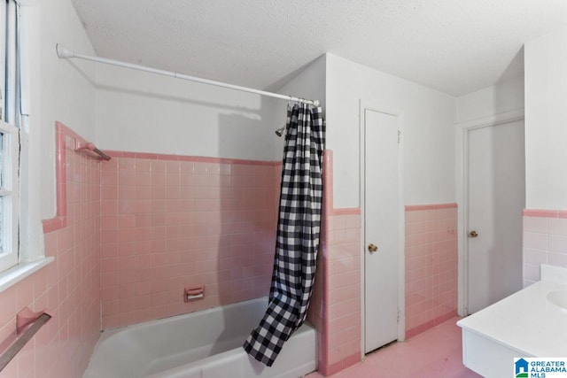bathroom featuring a wainscoted wall, a textured ceiling, shower / bath combo with shower curtain, and tile walls
