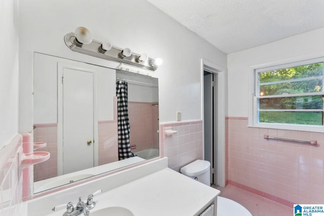 full bathroom with a textured ceiling, vanity, tile walls, a wainscoted wall, and toilet