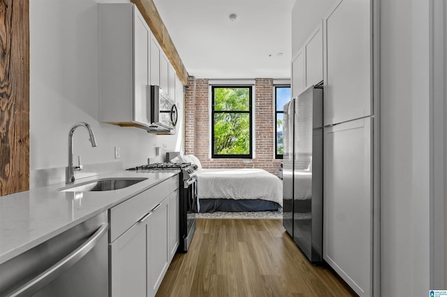 kitchen with light stone countertops, white cabinets, appliances with stainless steel finishes, wood finished floors, and a sink