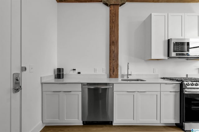 kitchen with white cabinets, a sink, light countertops, appliances with stainless steel finishes, and wood finished floors