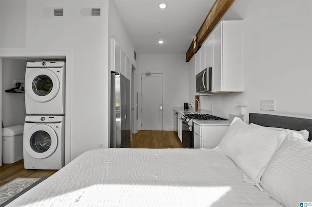 bedroom featuring visible vents, freestanding refrigerator, stacked washer / dryer, and wood finished floors